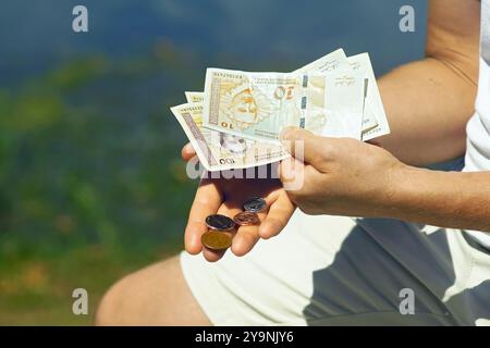 Der Mann hält Münzen von 1 bosnischer Wandelmarke, 50, 20 und 5 Fening in der einen Hand und Banknoten von 100 und 10 BAM in der anderen Hand. Stockfoto