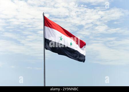 Flagge auf syrischem Flaggenmast und blauem Himmel, Flagge der Arabischen Republik Syrien flattert in blauem Himmel großes nationales Symbol. Die weiße jemenitische Flagge schwenkt, Independen Stockfoto