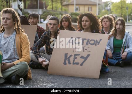 Gruppe verschiedener junger Menschen, die an einem Sit-in-Protest teilnehmen, mit einem Schild mit der Aufschrift „Action is the Key“. Das Bild erfasst Jugendaktivismus, Einheit, Stockfoto