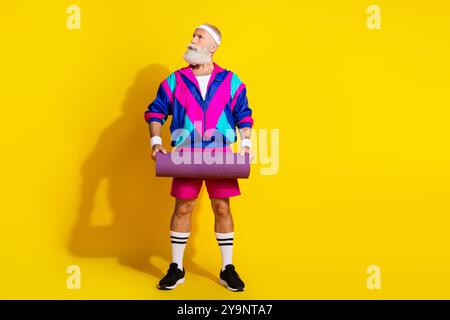 Foto-Banner in voller Länge des sportlichen fröhlichen alten Mannes halten Matte-Look leer Raum gekleidete Retro-Sportbekleidung isoliert auf gelbem Hintergrund Stockfoto