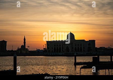 Wunderschöner Sonnenaufgang auf dem Meer in Sharjah. Wunderschöne Gebäude mit arabischer Architektur vor dem Hintergrund eines Abendsonnenverkehrs Stockfoto