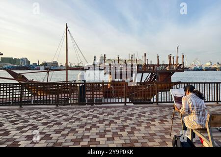 Eine Künstlerin malt ein altes Holzschiff auf dem Damm in Sharjah. Sharjah. Vereinigte Arabische Emirate, 28. Januar 2024. Stockfoto