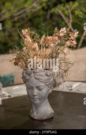 Ziervase in Form einer klassischen Göttin oder Figur, gefüllt mit getrockneten Blumen auf dem Tisch eines griechischen Restaurants oder einer Taverne als Dekoration. Stockfoto