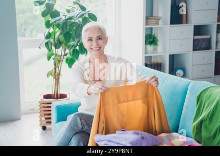 Foto von positiver hübscher Frau gekleideter weißer Cardigan, der das Haus reinigt, aufgeräumt, frische Kleidung, die drinnen verlegt wird Stockfoto