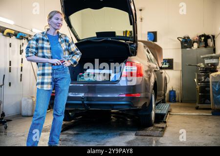 Weiblicher Mechaniker, der das Arbeitsgerät hält und am Eingang der Garage steht Stockfoto