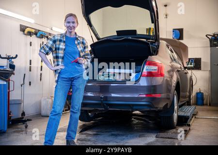 Weiblicher Mechaniker, der das Arbeitsgerät hält und am Eingang der Garage steht Stockfoto