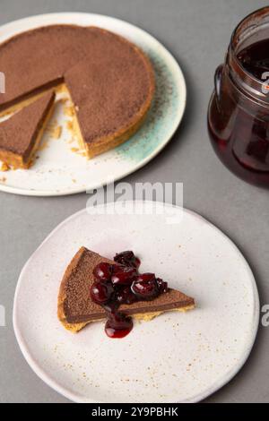 Ein Stück Schokoladenkuchen auf Einem Teller mit Kirschen und ganzer Torte Stockfoto