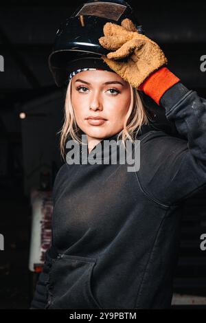 Frau in Arbeitshandschuhen und Schweißhelm, die eine Taschenlampe in einer Werkstatt hält Stockfoto