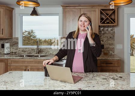 Eine Frau am Telefon, eine rote Tasse in der Hand, die in einer Küche steht Stockfoto