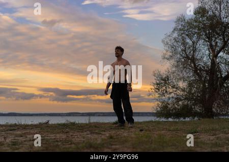 Ein Mann vor dem Hintergrund des Sonnenuntergangs am Ufer eines Sees. Stockfoto