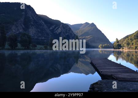 Ein hölzerner Dock über einem ruhigen und wunderschönen Bergsee an einem ruhigen Morgen mit Wolken, die aus dem Wasser steigen, in den spanischen Pyrenäen. Stockfoto