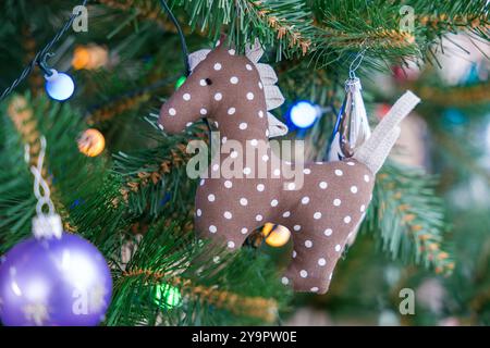 Handgefertigtes braunes Pferdeschmuck mit weißen Flecken, die an einem leuchtenden künstlichen Weihnachtsbaum hängen Stockfoto