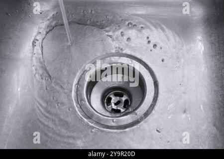 Wasser fließt aus einem Küchen- oder Badezimmerarmatur in ein Edelstahlwaschbecken. Stockfoto