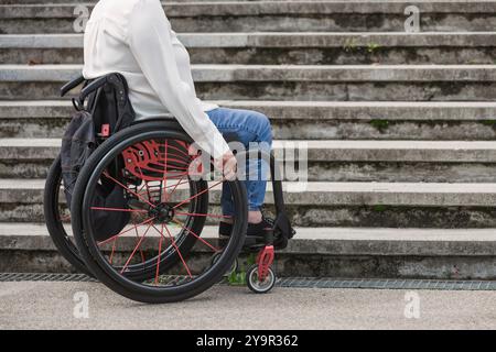 Frau im Rollstuhl hält an und wartet unten auf einer unzugänglichen Straßentreppe, die nicht hinaufgehen kann. Schwierigkeiten- und Behindertenkonzepte. Stockfoto