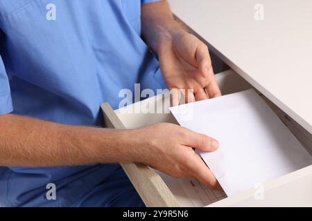 Korruptionskonzept. Doktor, der einen Umschlag mit Geld in die Schublade steckt, Nahaufnahme Stockfoto