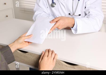 Korruptionskonzept. Frau, die dem Doktor am weißen Tisch einen Umschlag mit Geld gibt, Nahaufnahme Stockfoto