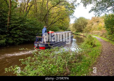 Mann auf einem Kanalschmalboot auf dem Caldon-Kanal, als er durch die Landschaft von Staffordshire in der Nähe von Cheddleton fährt Stockfoto