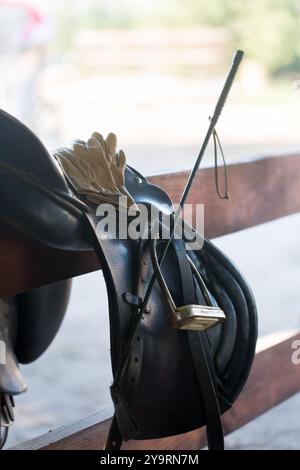 Ein Sattel auf einem Zaun mit Lederhandschuhen und einer Peitsche im Stall, Nahaufnahme Stockfoto