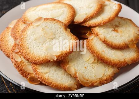 Mandeltuiles sind gebackene Waffeln, dünn, knusprig und süß mit Mandelcloseup auf dem Teller auf dem Tisch. Horizontal Stockfoto