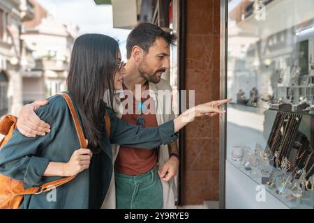 Junge schöne glückliche Paare, die verliebt sind, auf der Suche nach einer Verlobung oder einem Ehering durch das Straßenfenster des Juweliergeschäfts. Stockfoto