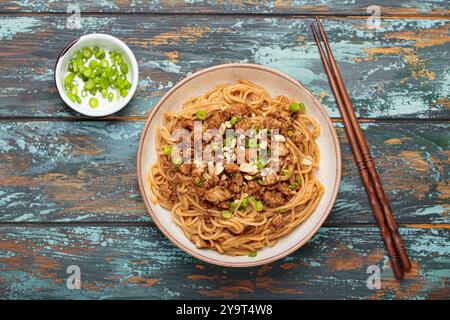 Dan Dan Dan Nudeln serviert mit Essstäbchen und grünen Zwiebeln von oben auf rustikalem Holztisch, traditionelles chinesisches Sichuan-Gericht Stockfoto