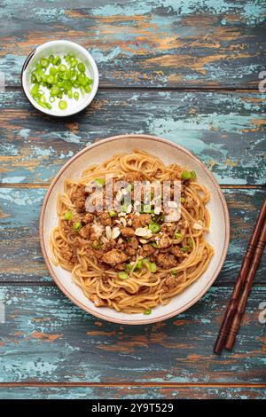 Dan Dan Dan Nudeln serviert mit Essstäbchen und grünen Zwiebeln von oben auf rustikalem Holztisch, traditionelles chinesisches Sichuan-Gericht Stockfoto