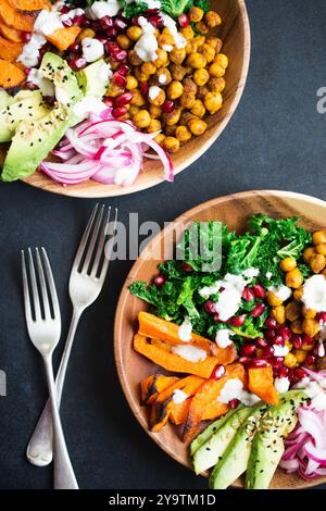 Warmer Wintersalat mit gebratenem Butternusskürbis, scharfen Kichererbsen, gedämpftem Grünkohl, Avocado und eingelegten roten Zwiebeln in Holzschüsseln. Stockfoto