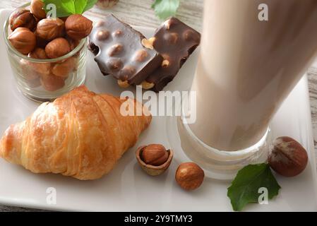 Detail der weißen Platte mit Glas mit Haselnussgetränk Croissant Schokolade mit Haselnüssen und Früchten. Draufsicht. Stockfoto