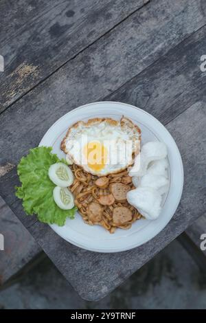 Gebratene indonesische Nudeln mit Ei, Wurst und frischem Gemüse auf rustikalem Tisch Stockfoto