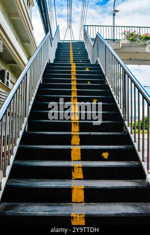 Treppenüberführungen für Personen, die die Straße sicher überqueren können. Gelbe Linien trennen die auf- und Abstiegswege. Edelstahlgeländer auf beiden Seiten. Stockfoto