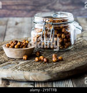 Ein Glas und eine Schüssel mit scharfen gerösteten Kichererbsen auf einem rustikalen Holzbrett. Stockfoto