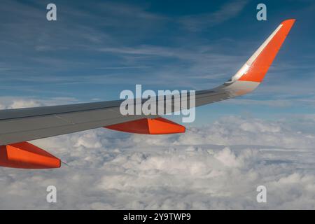 Der Flügel eines Flugzeugs gegen den blauen Himmel und eine Schicht weißer Wolken darunter Stockfoto