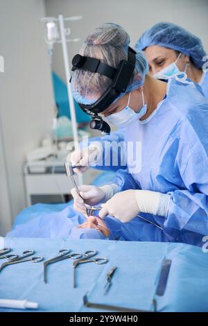 Chirurgische Krankenschwester assistierender Chirurg bei Ethyidektomie-Operation, Narkosepatient auf Operationstisch Stockfoto