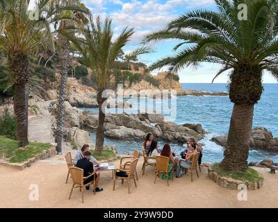 Lloret de Mar, Spanien - 18. September 2024: Menschen an Tischen ein gemütliches Café am Meer im Schatten von Palmen Stockfoto