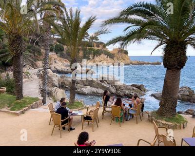 Lloret de Mar, Spanien - 18. September 2024: Menschen an Tischen ein gemütliches Café am Meer im Schatten von Palmen Stockfoto