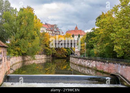 Nürnberger Stadtblick, 11.10.2024 Blick in Richtung Kasemattentor bei der Steubenbrücke in Nürnberg. Die Pegnitz wird von herbstlich gefärbten Bäumen gesäumt, und im Hintergrund ist eine historische, überdachte Holzbrücke zu sehen, die sich über den Fluss spannt. Dahinter steht das markante historische ADAC-Haus mit seinem roten Dach und charakteristischer Architektur. Nürnberg Bayern Deutschland *** Nürnberg Stadtansicht, 11 10 2024 Blick in Richtung Kasemattentor bei Steubenbrücke in Nürnberg die Pegnitz ist gesäumt von herbstlichen Bäumen und einer historischen überdachten Holzbrücke über den Fluss ca. Stockfoto