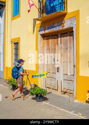 Ein Wanderer mit Rucksack und Wanderstöcken an den rustikalen Holztüren einer PilgerAlbergue auf der Jakobsweg. Spanien. Stockfoto