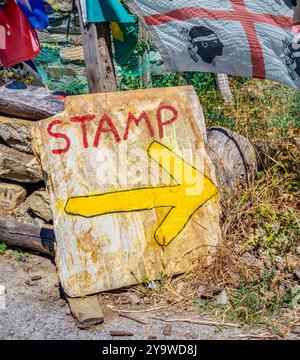 Ein Schild aus verwittertem Stein mit einem gelben Pfeil und dem Wort „STEMPEL“, das eine Stelle angibt, an der das Compostela-Dokument auf dem Jakobsweg abgestempelt werden soll. Stockfoto