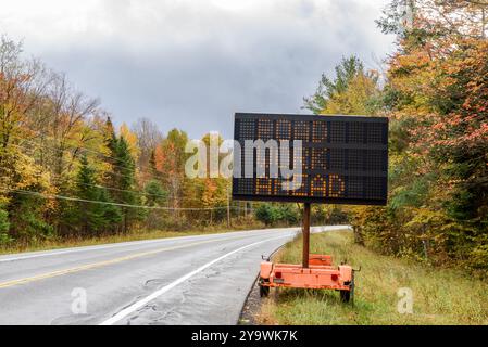 Elektronisches Straßenschild auf einem Anhänger, das an einem bewölkten Herbsttag auf einer Forststraße in den Bergen Bauarbeiten anzeigt Stockfoto