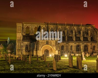 Oktober 2024. Malmesbury, Wiltshire, England - in einer kühlen Nacht erleuchtet die aurora den Nachthimmel über der historischen Abtei auf dem Cotswold Hügel Stockfoto