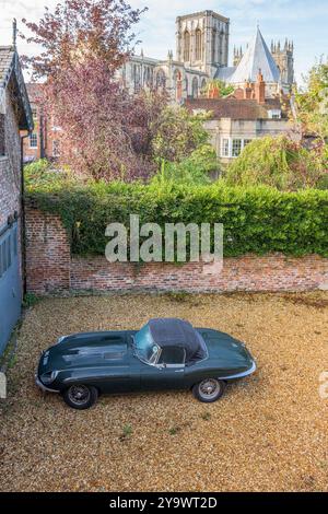 Vintage-Soft-Top, britischer Rennwagen, E-Typ Jaguar, der auf einem Schotterhof geparkt ist, und York Münster im Hintergrund. Stockfoto