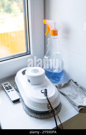 Fensterputzmittel liegen mit einem Lappen, Spray, Reinigungsmittel und einem Roboterreiniger auf der Fensterbank. Frühjahrsputz im Haus, Reinigungsdienst Stockfoto