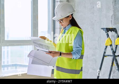 Frau in Schutzweste Schutzhelm mit Plan auf neuer Wohn- oder Gewerbeimmobilie Stockfoto