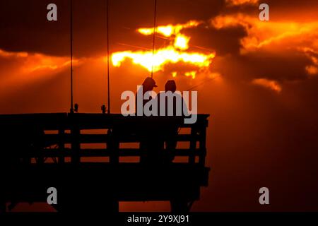 Isle Of Palms, Usa. Oktober 2024. Fischer, die von einem dramatischen Sonnenaufgang umgeben sind, werfen ihre Linien am Ende des Isle of Palms Pier am 11. Oktober 2024 in Isle of Palms, South Carolina. Hurrikan Milton zog 400 Meilen weiter nach Süden, führte aber herbstliches Wetter entlang der Küste, während die Stürme aufwachen. Quelle: Richard Ellis/Richard Ellis/Alamy Live News Stockfoto