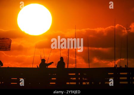 Isle Of Palms, Usa. Oktober 2024. Fisherman Silhouetten von einem dramatischen Sonnenaufgang werfen ihre Linien vor der Isle of Palms Pier am 11. Oktober 2024 in Isle of Palms, South Carolina. Hurrikan Milton zog 400 Meilen weiter nach Süden, führte aber herbstliches Wetter entlang der Küste, während die Stürme aufwachen. Quelle: Richard Ellis/Richard Ellis/Alamy Live News Stockfoto