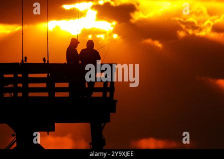 Isle Of Palms, Usa. Oktober 2024. Fischer, die von einem dramatischen Sonnenaufgang umgeben sind, werfen ihre Linien am Ende des Isle of Palms Pier am 11. Oktober 2024 in Isle of Palms, South Carolina. Hurrikan Milton zog 400 Meilen weiter nach Süden, führte aber herbstliches Wetter entlang der Küste, während die Stürme aufwachen. Quelle: Richard Ellis/Richard Ellis/Alamy Live News Stockfoto