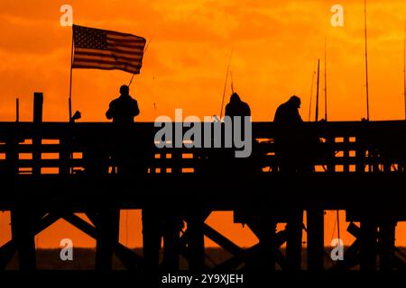 Isle Of Palms, Usa. Oktober 2024. Fisherman Silhouetten von einem dramatischen Sonnenaufgang werfen ihre Linien vor der Isle of Palms Pier am 11. Oktober 2024 in Isle of Palms, South Carolina. Hurrikan Milton zog 400 Meilen weiter nach Süden, führte aber herbstliches Wetter entlang der Küste, während die Stürme aufwachen. Quelle: Richard Ellis/Richard Ellis/Alamy Live News Stockfoto