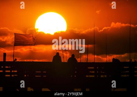 Isle Of Palms, Usa. Oktober 2024. Fisherman Silhouetten von einem dramatischen Sonnenaufgang werfen ihre Linien vor der Isle of Palms Pier am 11. Oktober 2024 in Isle of Palms, South Carolina. Hurrikan Milton zog 400 Meilen weiter nach Süden, führte aber herbstliches Wetter entlang der Küste, während die Stürme aufwachen. Quelle: Richard Ellis/Richard Ellis/Alamy Live News Stockfoto