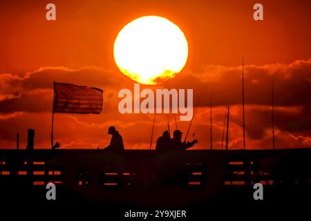 Isle Of Palms, Usa. Oktober 2024. Fisherman Silhouetten von einem dramatischen Sonnenaufgang werfen ihre Linien vor der Isle of Palms Pier am 11. Oktober 2024 in Isle of Palms, South Carolina. Hurrikan Milton zog 400 Meilen weiter nach Süden, führte aber herbstliches Wetter entlang der Küste, während die Stürme aufwachen. Quelle: Richard Ellis/Richard Ellis/Alamy Live News Stockfoto