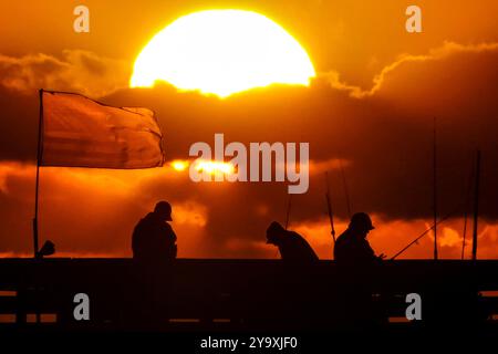 Isle Of Palms, Usa. Oktober 2024. Fisherman Silhouetten von einem dramatischen Sonnenaufgang werfen ihre Linien vor der Isle of Palms Pier am 11. Oktober 2024 in Isle of Palms, South Carolina. Hurrikan Milton zog 400 Meilen weiter nach Süden, führte aber herbstliches Wetter entlang der Küste, während die Stürme aufwachen. Quelle: Richard Ellis/Richard Ellis/Alamy Live News Stockfoto